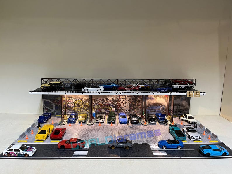 May include: A model car garage display with a variety of colorful cars, including red, blue, yellow, and white. The garage has a graffiti-style wall with the words "Eat Sleep Street" on it.