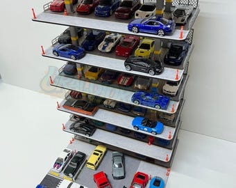 May include: A multi-level miniature parking garage filled with various toy cars. The cars are in different colors, including red, blue, black, and white. The garage has gray levels with yellow support beams and orange traffic cones.
