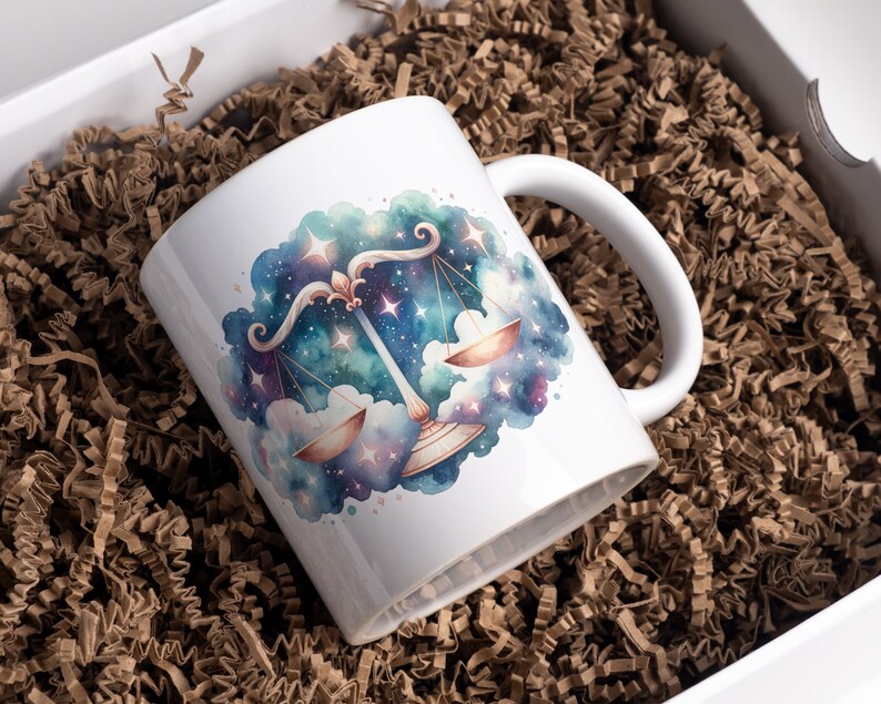 May include: White ceramic mug with a watercolor illustration of the Libra zodiac sign in a galaxy setting. The scales are gold and the background is a blue and purple nebula with stars.