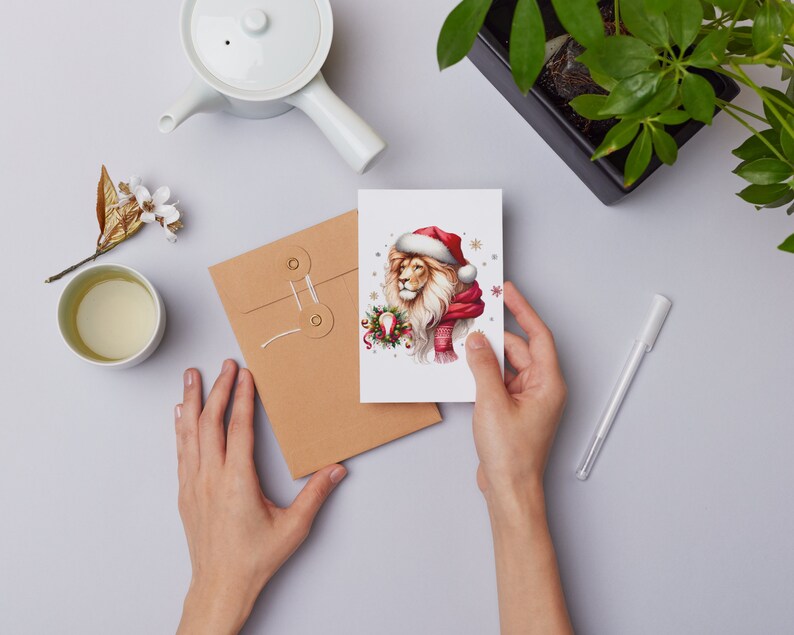 Puede incluir: Una tarjeta de Navidad con un le&oacute;n que lleva un gorro de Pap&aacute; Noel y una bufanda roja. El le&oacute;n est&aacute; rodeado de copos de nieve y acebo.