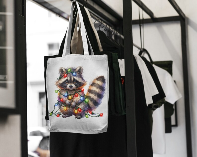 May include: White tote bag featuring a cartoon raccoon adorned with colourful Christmas lights. The raccoon is standing against a white backdrop.