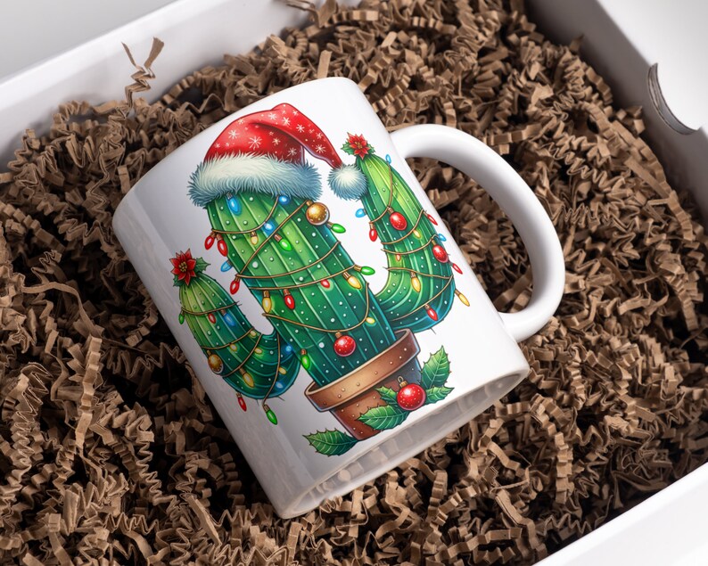 Op de afbeelding: Witte keramische mok met een kerstcactusontwerp. De cactus is versierd met een kerstmanmuts en kerstverlichting.
