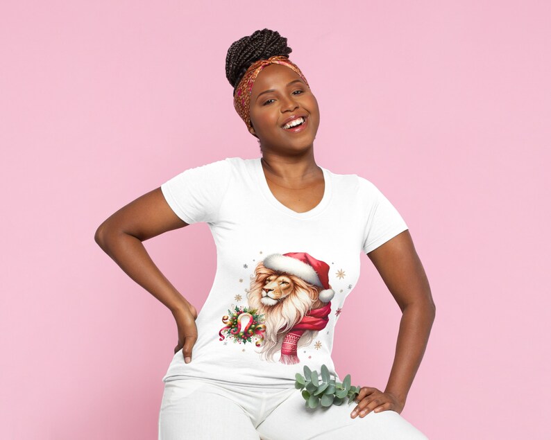 Puede incluir: Una camiseta blanca con un le&oacute;n festivo que lleva un gorro de Pap&aacute; Noel y una bufanda. El le&oacute;n est&aacute; rodeado de acebo y copos de nieve.