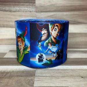 May include: A roll of blue grosgrain ribbon featuring a repeating graphic print of Peter Pan, Captain Hook, Tinker Bell, and Wendy Darling against a night sky background with a silhouette of a pirate ship and a crocodile in the water.