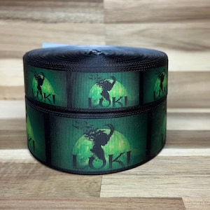 May include: A roll of black grosgrain ribbon featuring a repeating graphic print of a green circular moon and a dark silhouette figure with the text LOKI printed in black capital letters centered below the graphic on the green background.