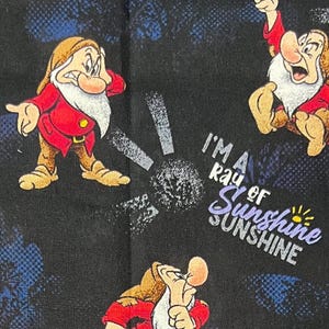 May include: Black fabric featuring cartoon images of a dwarf in a red coat and the text "I'm a ray of sunshine". The dwarf has a white beard and is in various poses. The background has blue and white accents.