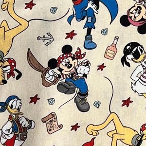 Puede incluir: Tela color crema con un patrón repetido de personajes piratas de dibujos animados, incluyendo Mickey Mouse, Donald Duck y Goofy. El diseño incluye símbolos piratas como mapas del tesoro, anclas y estrellas rojas, con una botella de ron.