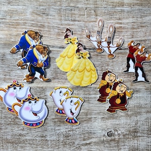Puede incluir: Un conjunto de diez adornos para pasteles imprimibles con personajes de la película de Disney La Bella y la Bestia. Los adornos incluyen a Bella, Bestia, Din Don, Lumière, Señora Tetera, Chip y la rosa encantada.