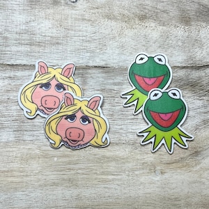 May include: Four colorful iron-on patches featuring Miss Piggy and Kermit the Frog from the Muppets. The patches are perfect for adding a touch of whimsy to clothing, bags, or other accessories.