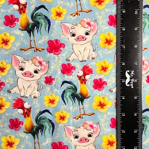 May include: A blue fabric with a repeating pattern of a white pig with a flower crown and a rooster with a red comb. The fabric is measured with a ruler in inches.