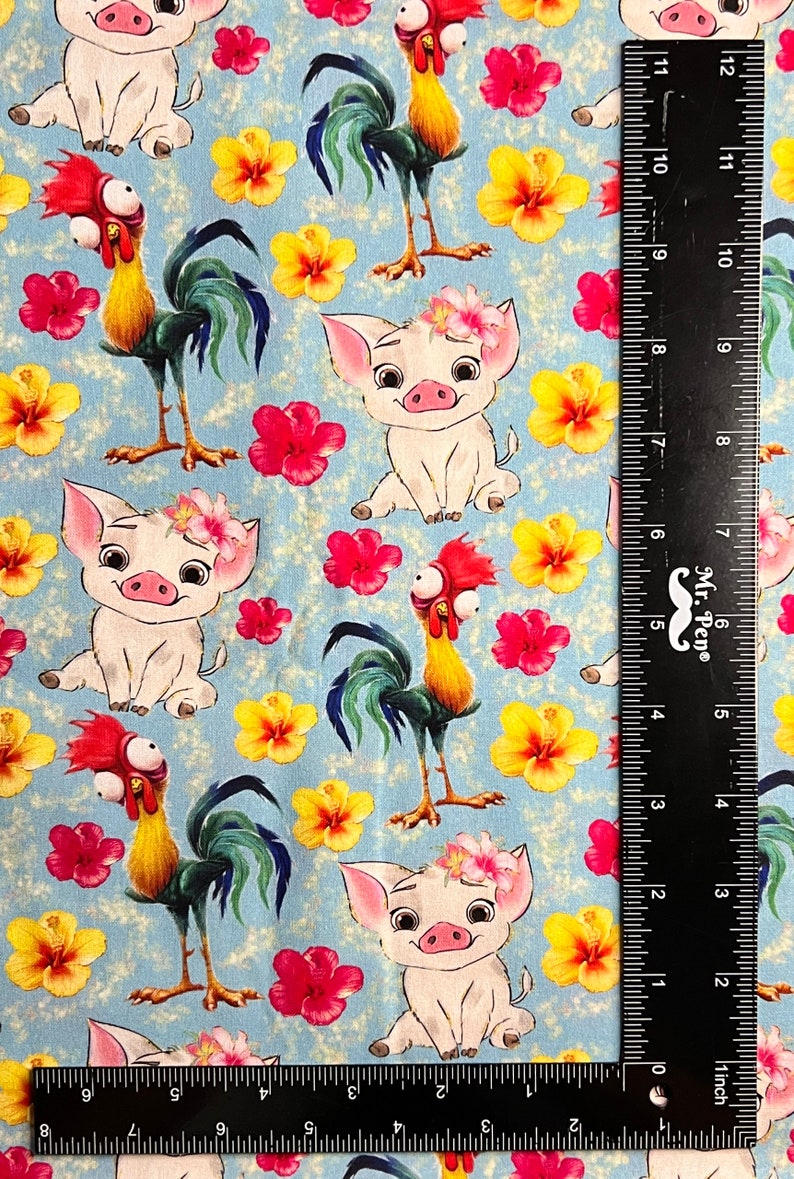 May include: A blue fabric with a repeating pattern of a white pig with a flower crown and a rooster with a red comb. The fabric is measured with a ruler in inches.