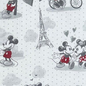 May include: A white fabric with a repeating pattern of Mickey Mouse and Minnie Mouse in black and white with red accents. The pattern also includes the Eiffel Tower and hearts. The background is a white fabric with small gray dots.