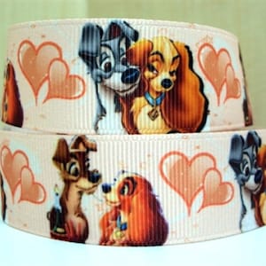May include: A pink ribbon with a repeating pattern of Lady and the Tramp characters and hearts. The ribbon is made of satin and has a shiny finish.