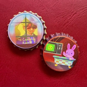 Puede incluir: Dos pines circulares con forma de chapa y bordes dentados. El pin izquierdo muestra a una persona en una ventana con el texto Fox Counseling Room. El pin derecho presenta un conejo rosa en una bañera a cuadros junto a un televisor.
