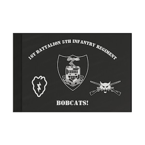 Pode incluir: Bandeira preta e branca com o texto "1st Battalion 5th Infantry Regiment" e "Bobcats!" Um escudo com um raio e rifles cruzados com uma cabeça de lince também estão na bandeira.