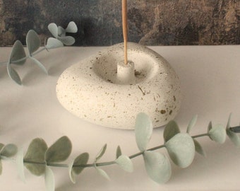 May include: White ceramic incense holder shaped like a heart with a speckled finish and gold flecks. A wooden incense stick is placed in the holder.