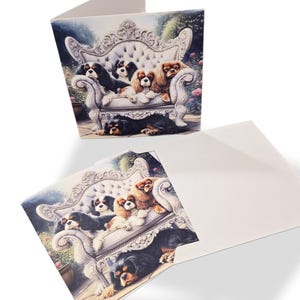 May include: Greeting card featuring a watercolor illustration of Cavalier King Charles Spaniels on a white ornate sofa. The dogs are in various colors, including black, brown, and white. The card is open, revealing a blank interior.