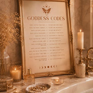 Pode incluir: Uma impressão emoldurada intitulada GODDESS CODES com uma ilustração de borboleta e uma lista de afirmações. A moldura dourada ornamentada repousa sobre uma superfície de mármore ao lado de um frasco de perfume, bandeja de mármore e velas.