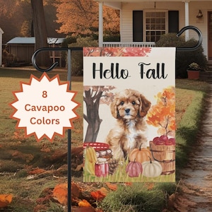 May include: A rectangular garden flag featuring the text Hello Fall in black script. The illustration depicts a brown and white Cavapoo puppy sitting in grass surrounded by pumpkins, a wooden bucket of apples, and autumn trees with orange leaves.