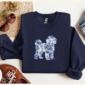 May include: Navy blue sweatshirt featuring a white and blue floral dog silhouette. The sweatshirt has a crew neck and long sleeves. The word "Navy" is printed in a white, cursive font in the lower left corner.