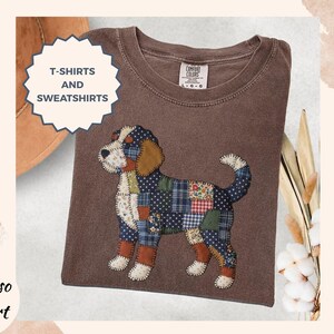 May include: Espresso-colored t-shirt with a patchwork dog design. The dog features patches of blue, green, and red fabric. The shirt also has the text "T-SHIRTS AND SWEATSHIRTS" in a white, starburst-shaped design.