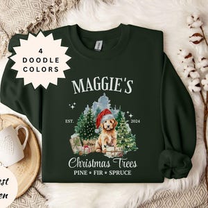 May include: Forest green sweatshirt with a graphic featuring a golden retriever wearing a Santa hat, surrounded by Christmas trees and gifts. The text reads "Maggie's Christmas Trees" with "Est. 2024". Includes a white starburst with "4 Doodle Colors".