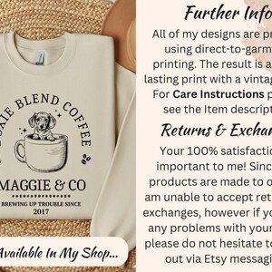 May include: Cream-colored sweatshirt featuring a dachshund dog in a coffee cup, with the text "Doxie Blend Coffee" and "Maggie & Co Brewing Up Trouble Since 2017." The design is printed on the front.