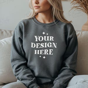 May include: A dark gray sweatshirt with the text "YOUR DESIGN HERE" in white lettering. The sweatshirt has a crew neck and long sleeves.