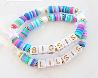 Puede incluir: Dos pulseras elásticas hechas de cuentas de arcilla planas y coloridas en tonos azul, rosa y verde, con cuentas espaciadoras doradas y dijes de estrellas transparentes. Una pulsera tiene cuentas blancas con BIG SIS y la otra LIL SIS.