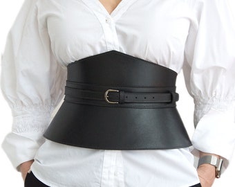 May include: A wide black leather corset belt with a silver buckle. The belt is worn over a white button-down shirt.