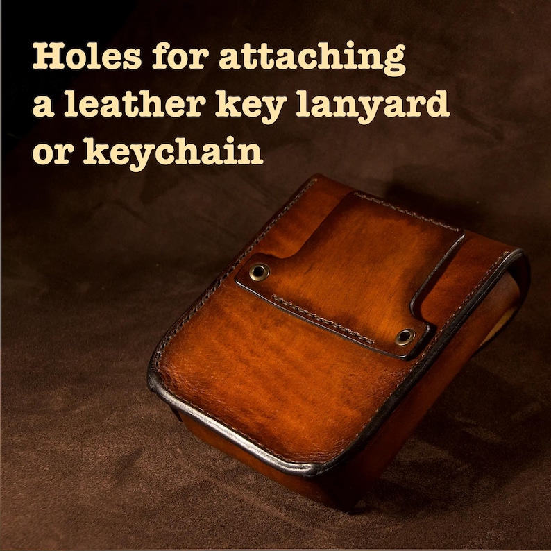 May include: A brown leather case with a flap and two holes for attaching a key lanyard or keychain. The case has a rich, textured appearance and is likely handmade. The text "Holes for attaching a leather key lanyard or keychain" is visible.