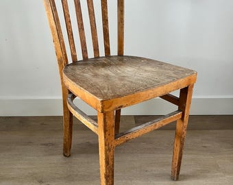 May include: A vintage wooden chair with a curved backrest and vertical slats. The seat and frame show signs of wear, with a distressed finish. The chair has four legs and is made of light brown wood.