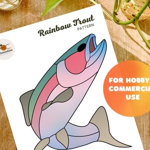 Può includere: Un'illustrazione colorata di una trota iridea, con uno schema di colori rosa, blu e verde. L'immagine è etichettata "Rainbow Trout Pattern" e "For Hobby + Commercial Use".