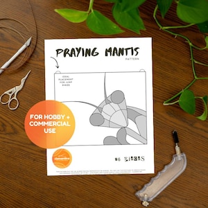 May include: A craft pattern titled "Praying Mantis" with a diagram, scissors, a craft knife, and a cutting tool on a wooden surface. The pattern includes the text "Ideal Placement for Jump Rings" and "For Hobby + Commercial Use."