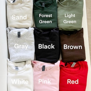 Puede incluir: Se muestran nueve sudaderas de cuello redondo en varios colores. Los colores incluyen arena, verde bosque, verde claro, gris, negro, marr&oacute;n, blanco, rosa y rojo. Cada sudadera tiene el nombre del color impreso debajo.