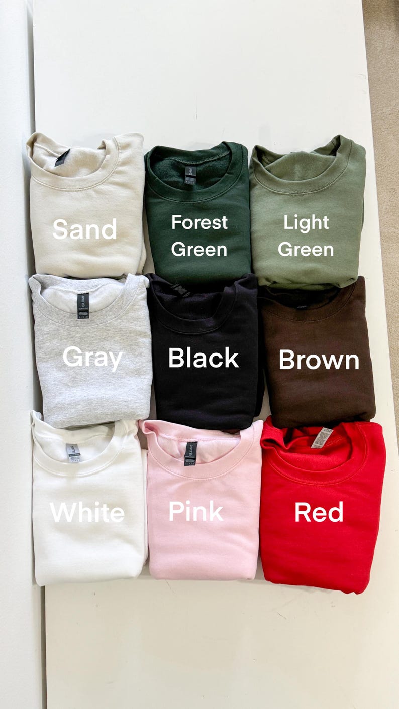 Puede incluir: Se muestran nueve sudaderas de cuello redondo en varios colores. Los colores incluyen arena, verde bosque, verde claro, gris, negro, marr&oacute;n, blanco, rosa y rojo. Cada sudadera tiene el nombre del color impreso debajo.