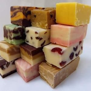 May include: A stack of assorted fudge squares in various flavours, including chocolate, vanilla, and fruit. The fudge is arranged in a pyramid shape, with the largest squares at the bottom and the smallest squares at the top.