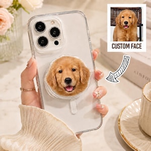 May include: A clear smartphone case featuring a circular pop-out grip with a printed golden retriever puppy face. The design includes a small inset graphic of the same puppy with the text CUSTOM FACE and a hand-drawn arrow pointing to the grip.