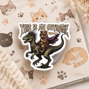 May include: A sticker featuring a cat wearing sunglasses and a crown, riding a green dinosaur. The sticker has the text "THIS IS AN OUTRAGE" in a stylized font. The background has cat-themed illustrations.
