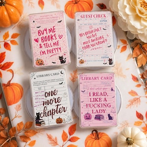May include: Four rectangular acrylic blocks featuring printed designs. Top left: pink grid with text 'BUY ME BOOKS & TELL ME I'M PRETTY'. Top right: white guest check with 'HEY BEAUTIFUL! YOU ARE MORE AMAZING THAN YOU KNOW!!'. Bottom left: library card with 'one more chapter'. Bottom right: library card with 'I READ, LIKE A FUCKING LADY'.