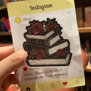 May include: A clear sticker featuring a stack of books with red roses and a candle. The sticker is designed to look like an Instagram post, with the word "Instagram" at the top and the text "Album. Thank you for liking it #Share daily life #Today #Delicacy" at the bottom.
