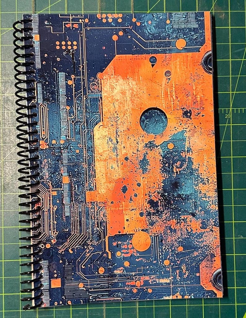 Puede incluir: Cuaderno con espiral con un dise&ntilde;o de placa de circuito. La cubierta presenta un patr&oacute;n abstracto azul y naranja que se asemeja a componentes electr&oacute;nicos. El cuaderno tiene una encuadernaci&oacute;n en espiral negra.