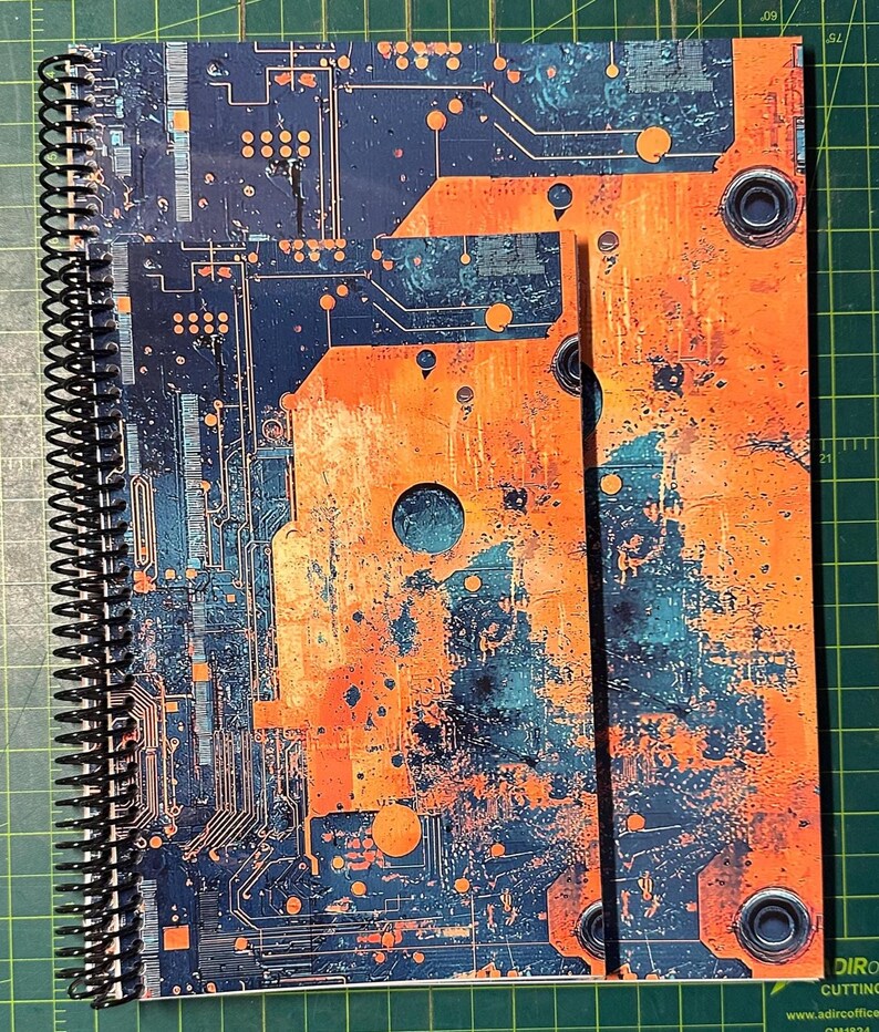 Puede incluir: Un cuaderno con espiral con un dise&ntilde;o vibrante de placa de circuito en tonos naranja, turquesa y azul marino. La cubierta muestra intrincados caminos y componentes electr&oacute;nicos, creando una est&eacute;tica inspirada en la tecnolog&iacute;a.