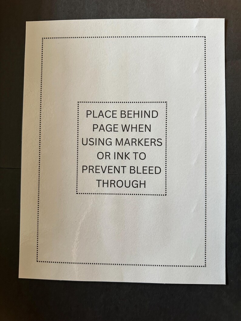 K&ouml;nnte beinhalten: Ein wei&szlig;es Blatt Papier mit einem schwarzen Rand und dem Text "PLACE BEHIND PAGE WHEN USING MARKERS OR INK TO PREVENT BLEED THROUGH" in der Mitte.