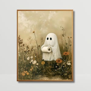 May include: A framed wall art print featuring a white ghost figure draped in a sheet, holding a roll of white toilet paper. The ghost is positioned in a field of wildflowers with muted earth tones, including orange, brown, and cream colours.