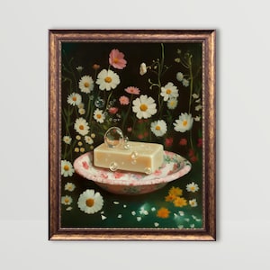 以下が含まれることがあります： 額縁に入った絵画で、花柄のボウルに入った石鹸が、デイジーと泡に囲まれて描かれています。このアートワークは、暗い背景と金色のフレームで、ヴィンテージな美学を作り出しています。石鹸は薄いベージュ色です。