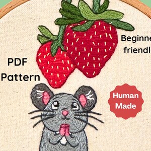 Può includere: Design ricamato con due fragole rosse con foglie verdi sopra un topo grigio con orecchie e zampe rosa. Il testo include "PDF Pattern", "Beginner friendly" e "Human Made".