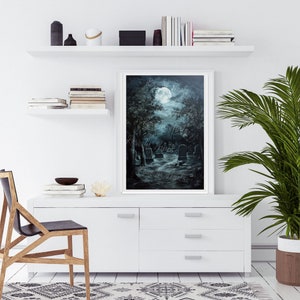 May include: A painting of a moonlit graveyard with a full moon in the sky. The trees are dark and the tombstones are white. The painting is framed in a white frame and is hanging on a white wall.