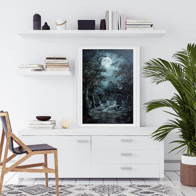 May include: A painting of a moonlit graveyard with a full moon in the sky. The trees are dark and the tombstones are white. The painting is framed in a white frame and is hanging on a white wall.