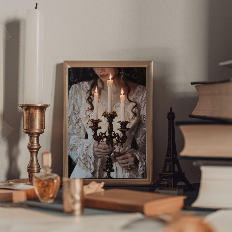 May include: A framed print of a woman in a white dress holding a candelabra with lit candles. The woman is looking down at the candles. The print is in a gold frame and is hanging on a wall.